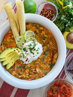 a white bowl filled with food next to bowls of salsa and tortilla chips