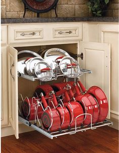 an open cabinet with many red pots and pans in the bottom rack on it