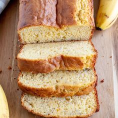 sliced loaf of banana bread sitting on top of a cutting board next to two bananas