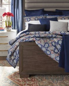 a bed with blue and white comforters in a bedroom next to a window filled with flowers