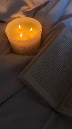 an open book sitting on top of a bed next to a lit candle