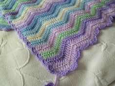 a crocheted blanket is laying on top of a white bed sheet with purple, green and blue stripes