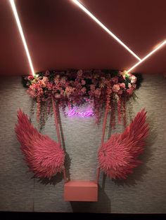 an arrangement of pink feathers and flowers on display in a room with lights above it