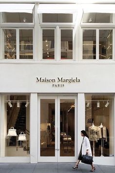 a woman walking past a store front with mannequins on display in the windows