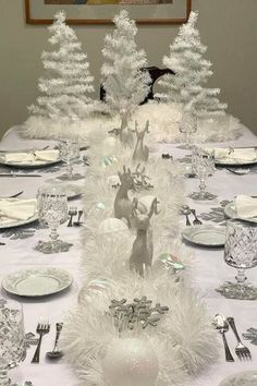 the table is set for christmas dinner with white decorations and silver cutlers on it