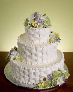 a three tiered white cake with flowers on it sitting on a table next to a wall