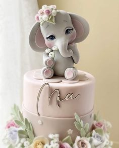 a pink and white cake with an elephant on top that says maa surrounded by flowers