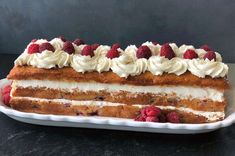 a large cake with white frosting and raspberries on top is sitting on a plate