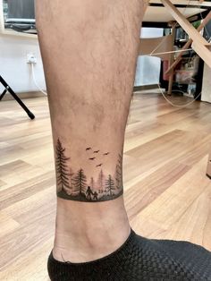 a man's foot with a small forest scene tattoo on the left side of his leg