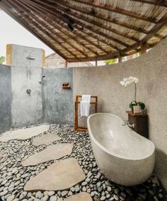 a large bathtub sitting under a wooden roof next to a stone covered bathroom floor