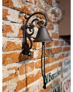 a wall mounted light on the side of a brick building with a metal bell attached to it