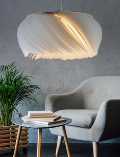 a white lamp hanging over a table next to a gray chair and potted plant