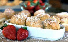 some pastries and strawberries are in a white bowl on a table with powdered sugar