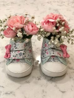 two baby shoes with flowers in them sitting on a marble counter top next to each other