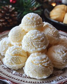 a white plate topped with lots of powdered sugar covered donuts next to a bowl of pine cones