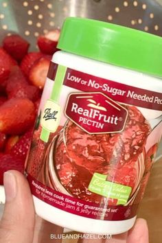 a hand holding a jar of realfruit fectin next to strawberries