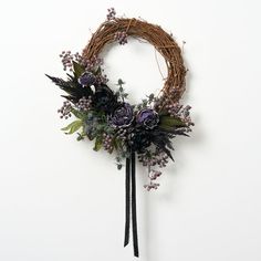 a wreath with purple flowers and greenery hanging on a wall