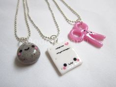 two necklaces with different designs on them sitting next to each other, one has a pink bow and the other is a gray cat