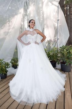 a woman in a white wedding dress standing on a wooden deck next to potted plants