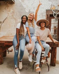 three women sitting at a picnic table with their arms in the air and one pointing