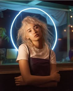 a woman standing with her arms crossed in front of a neon circle on the wall