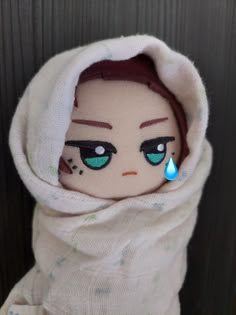 a stuffed doll wearing a white hoodie with green eyes and blue tear on it's nose