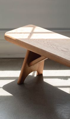 a wooden bench sitting on top of a floor next to a white wall with sunlight coming through the window