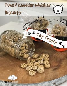 cat treats are sitting on top of a cutting board with a sign that says tuna and cheddar whisker biscuits