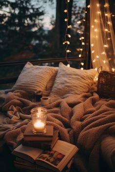 a lit candle sits on top of a bed with books and blankets in front of a window