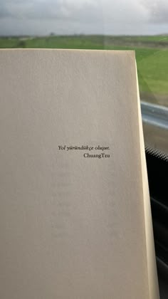 an open book sitting on top of a window sill next to a green field