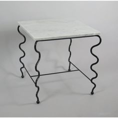 a white marble table with black iron legs and an intricate design on the top, against a gray background