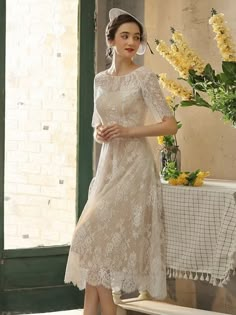 a woman in a dress and hat standing next to a table with flowers on it