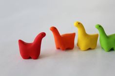 three small plastic ducks sitting next to each other on a white surface, one is yellow and the other two are red