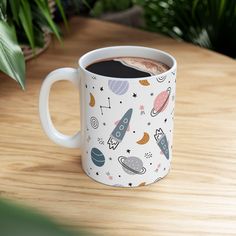 a white coffee mug with an outer space pattern on it sitting on a wooden table