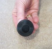 a person's hand holding a black object in the middle of their fingers on carpet