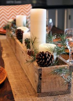 a wooden box filled with pine cones and candles on top of a dining room table