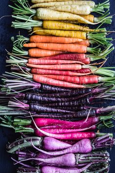 an array of carrots and radishes laid out in a row on a black surface