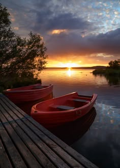 two red canoes sitting on top of a wooden dock next to the ocean at sunset