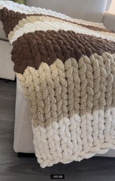 a white couch sitting next to a brown and white blanket on top of a wooden floor