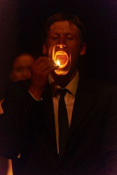 a man in a tuxedo is holding a lit candle up to his mouth