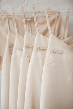 four white aprons hanging on a rack with personalized embroidered names and name written on them