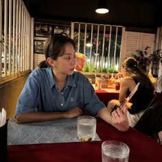 two people sitting at a table with drinks and papers in front of them, one woman is holding a cell phone