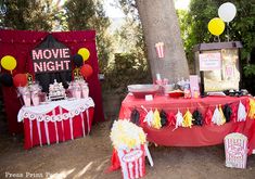 an outdoor movie night party with popcorn, cake and decorations on the table in front of a tree