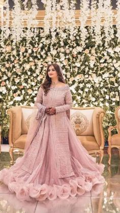 a woman in a pink lehenga standing next to some flowers and greenery