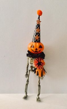 an orange and black halloween decoration with a pumpkin on it's head, standing in front of a white wall