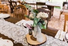 the table is set with white and pink flowers in a vase on top of a wooden slice