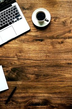 an open laptop computer sitting on top of a wooden table next to a cup of coffee