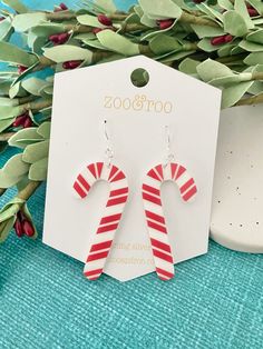 red and white candy cane earrings on top of a blue table next to green leaves