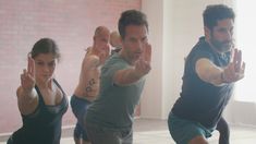 a group of people doing exercises in an empty room with one man pointing at the camera