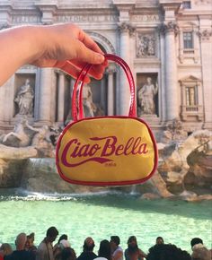 a hand holding a bag with the word cia bella in front of a fountain